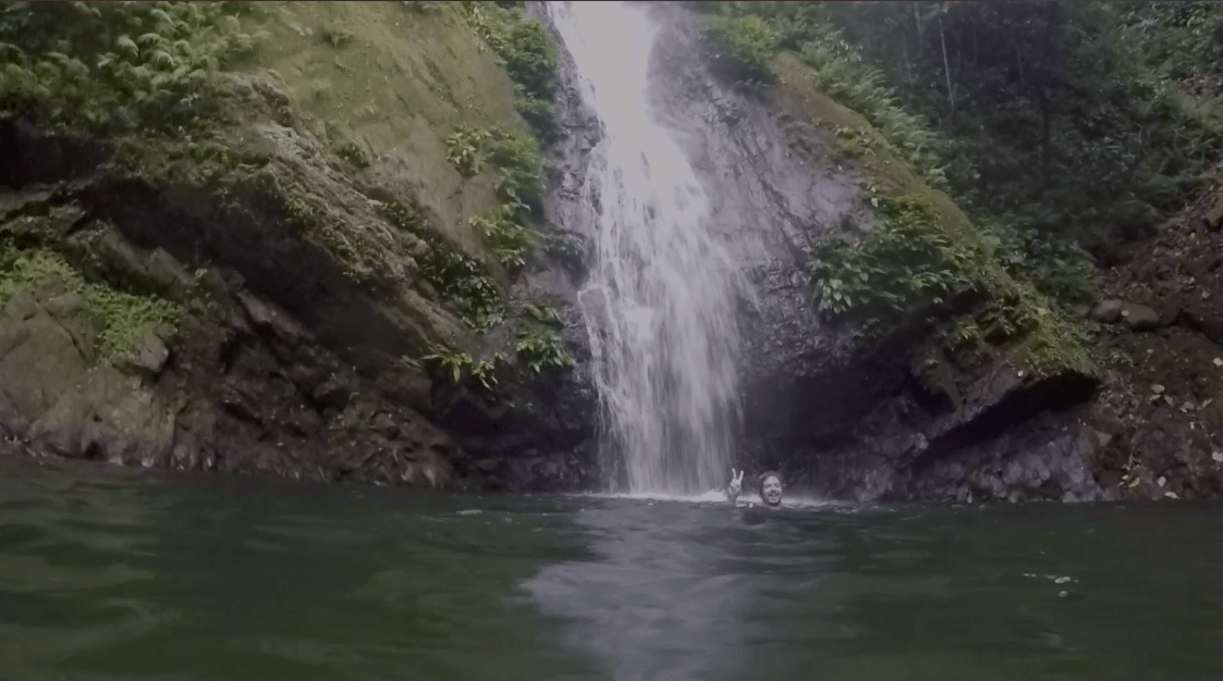 Lenny through paradise swimming in the kabigan falls waterfall in pagudpud ilocos norte philippines and doing the peace sign gesture